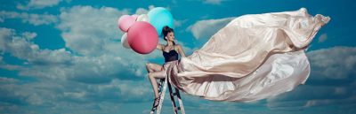 Frau sitzt mit bunten Ballons in der Hand auf einer Leiter auf einem Flugplatz