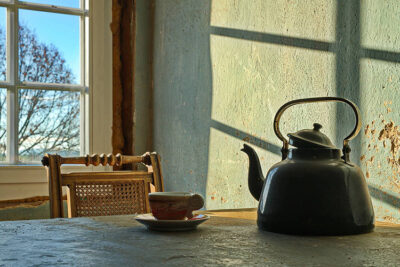 Stilleben mit einer Teekanne und Teetasse und Sonnenlicht das durch ein Fenster im Hintergrund scheint